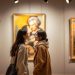 Couple asiatique discutant devant des tableaux dans une salle de musée, éclairage tamisé et spot lumineux, expressions naturelles, ambiance chaleureuse et intime