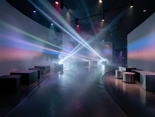 Salle d’exposition immersive élégante, avec parcours au sol, projections lumineuses et mobilier scénographique moderne dans une ambiance cinématographique.