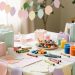 Table de fête aux couleurs pastel avec guirlandes en papier, cadeaux et activités créatives adaptées aux bébés.